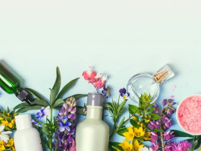 Bottles and tinctures for beauty alchemy amongst colorful flora on blue background