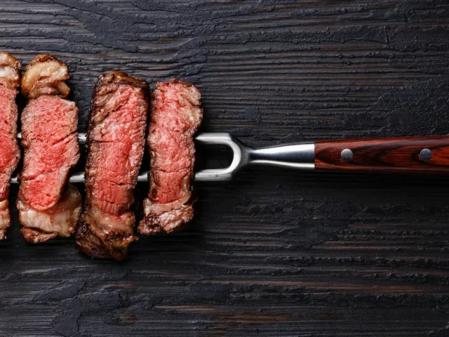 4 pieces of steak on pitchfork on dark wooden table