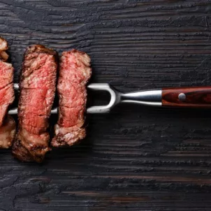 4 pieces of steak on pitchfork on dark wooden table