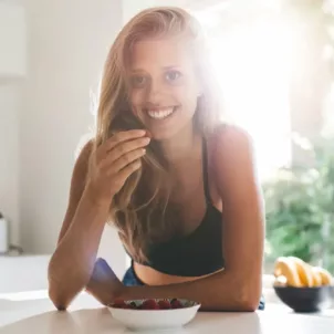 Fit blonde woman smiling in kitchen eating berries and healthy food to lose weight