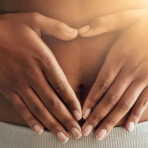 Dark skinned woman with hands over her stomach with light trickling in through window