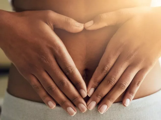 Dark skinned woman with hands over her stomach with light trickling in through window