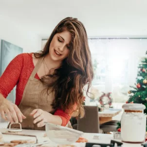 Woman in kitchen preparing cookies for the holidays with Christmas tree in background