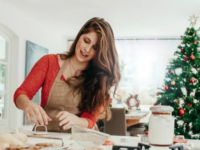 Woman in kitchen preparing cookies for the holidays with Christmas tree in background