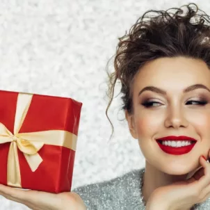 Woman with dramatic red lipstick holding a red-wrapped holiday gift with silver background