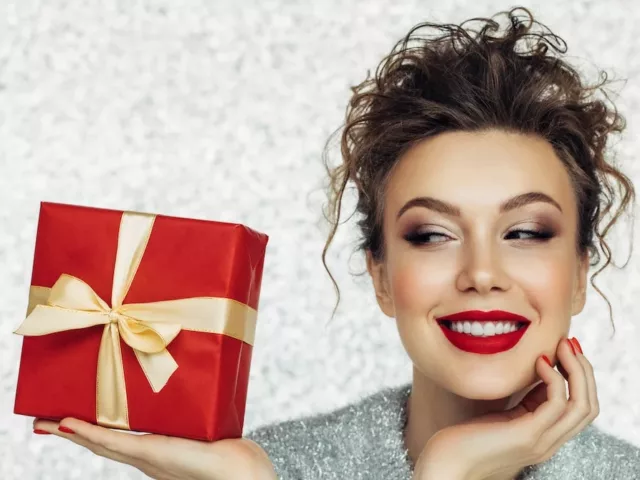 Woman with dramatic red lipstick holding a red-wrapped holiday gift with silver background