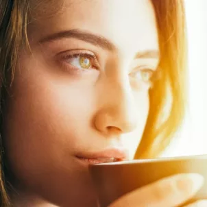 Woman looking pensive out the window drinking a mug of natural detox turmeric