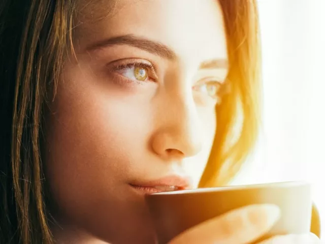 Woman looking pensive out the window drinking a mug of natural detox turmeric