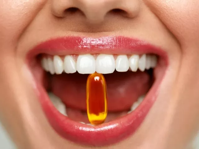 Close-up shot of woman's mouth holding a vitamin for skin in between her teeth