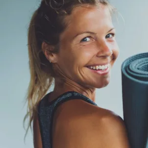 Blonde woman with an energy boost holding yoga mat looking back and smiling