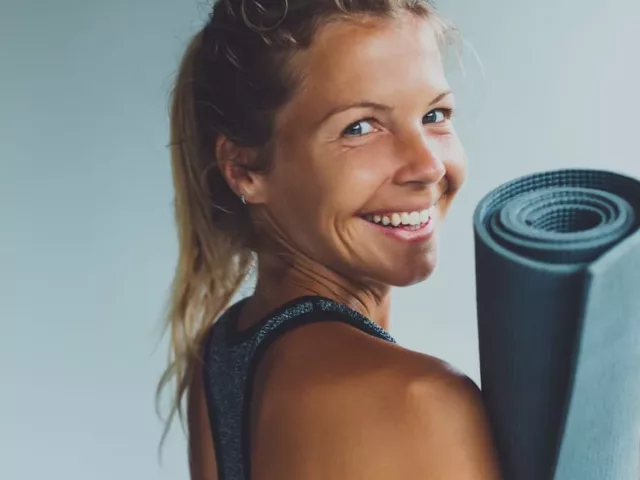 Blonde woman with an energy boost holding yoga mat looking back and smiling