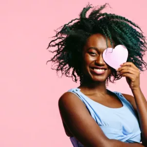 Single woman holding paper heart to her face on pink background