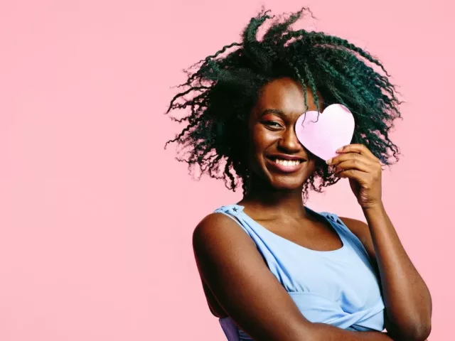 Single woman holding paper heart to her face on pink background