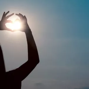 Back shot of woman holding her hands in a heart shape to the sun for vitamin D