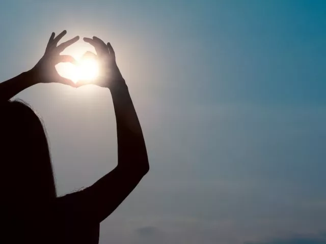 Back shot of woman holding her hands in a heart shape to the sun for vitamin D