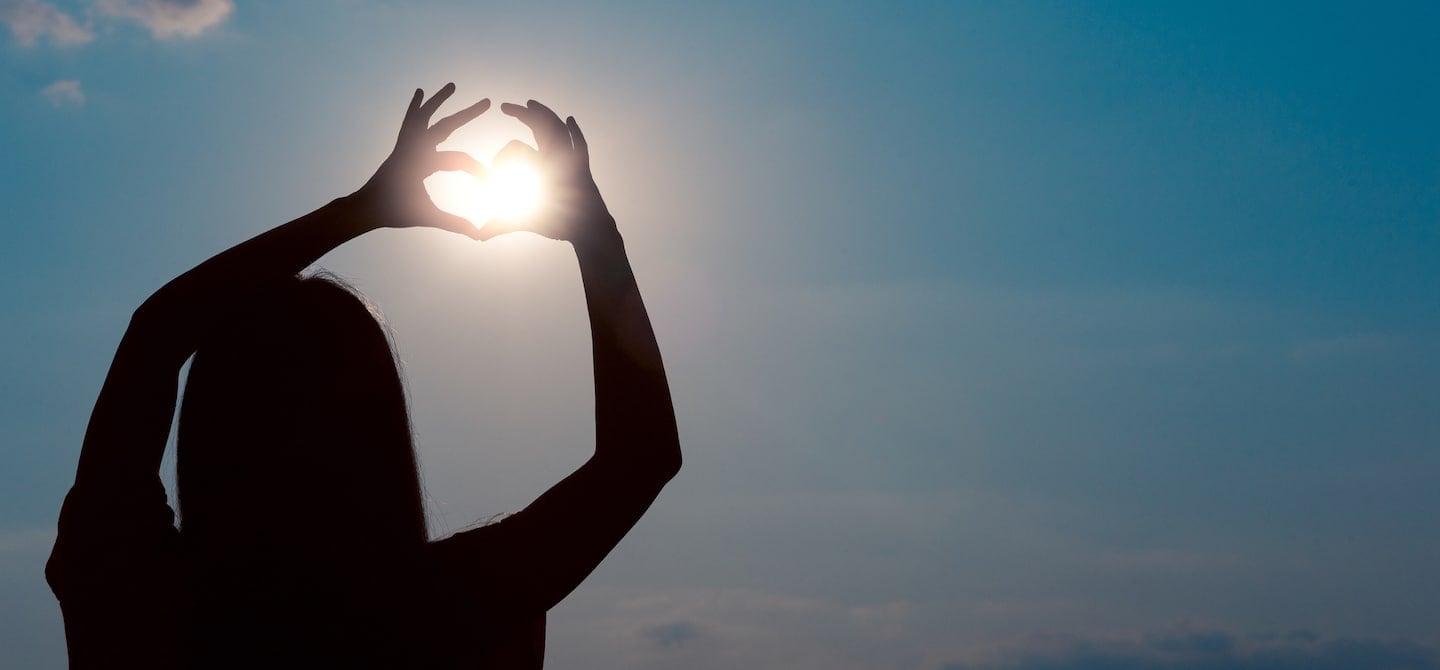 Back shot of woman holding her hands in a heart shape to the sun for vitamin D