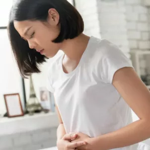 Woman in bed holding hands to her stomach in pain because she needs digestive enzymes to stop bloating