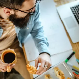 Man eating pastries and coffee by his desk and laptop to illustrate the gut-brain axis connection