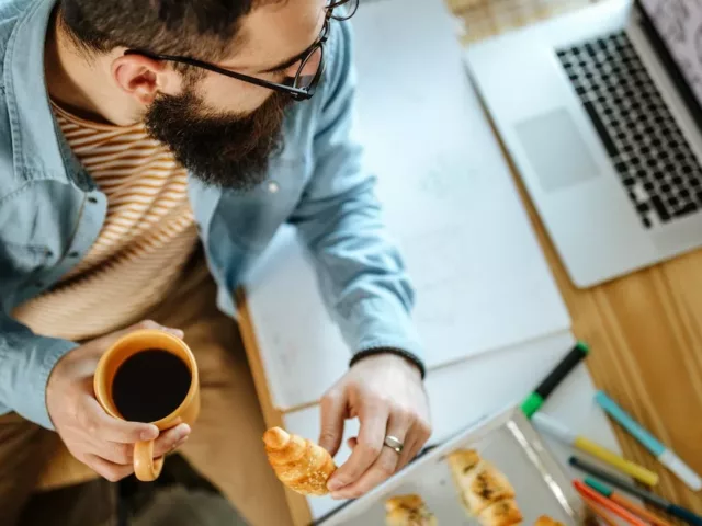 Man eating pastries and coffee by his desk and laptop to illustrate the gut-brain axis connection