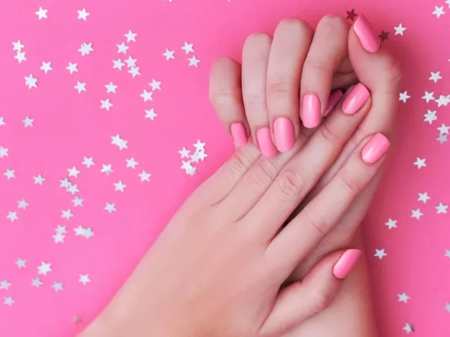 Woman's hands with pink nail polish on pink background after taking the best vitamins for nails