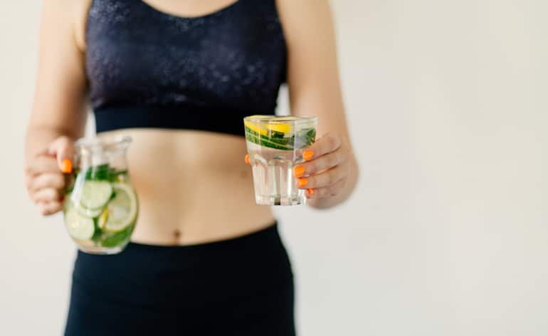 Fit woman who quit sugar holding Infused Water with Lemon and Cucumber