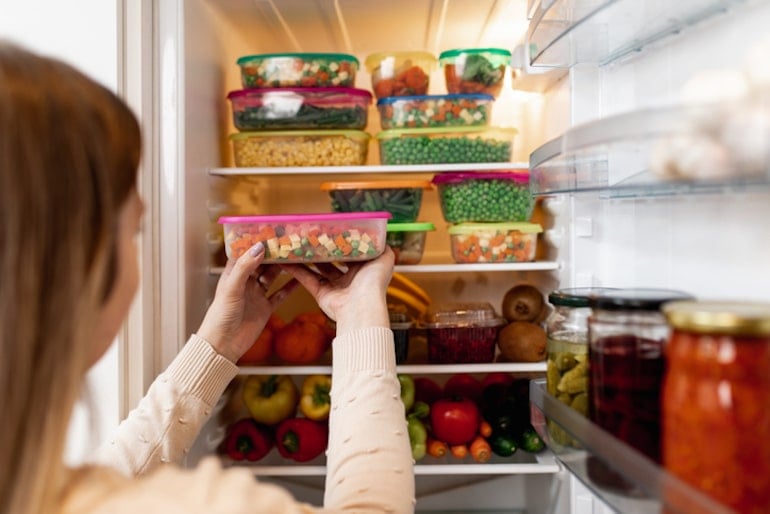 Woman on a no sugar diet putting meal prep containers of veggies into fridge