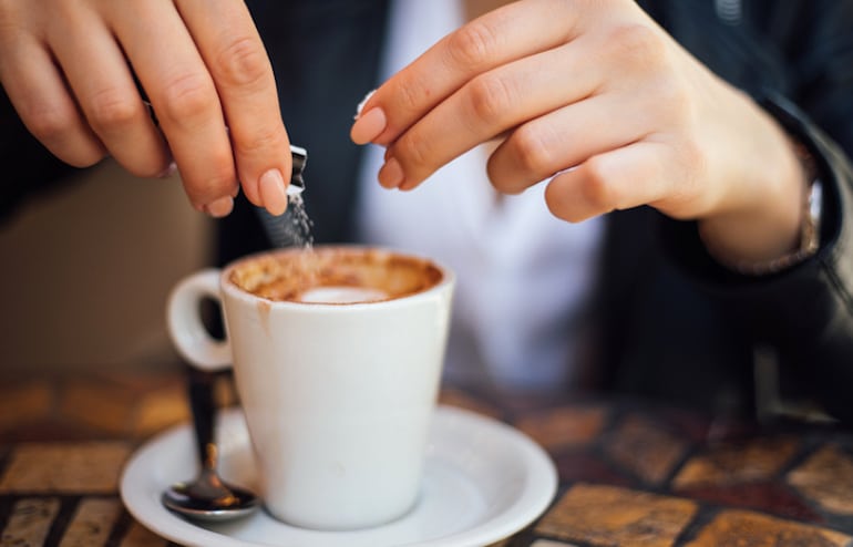 Woman adding sugar packet to coffee to illustrate why sugar is bad for your health