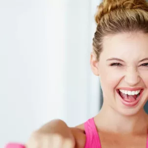 Woman in pink athletic gear smiling while raising dumbbells because she reached her happy weight