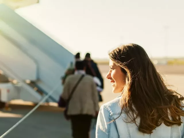 Woman on tarmac looking into the sun about to board an airplane