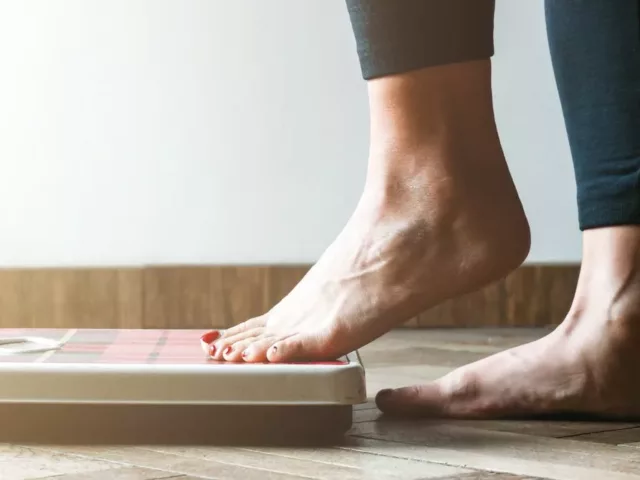 Woman following an extreme diet plan stepping onto scale to check her rapid weight loss