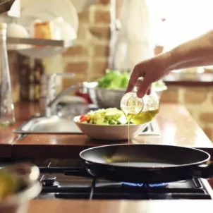 Woman pouring oil with healthy fat into a skillet