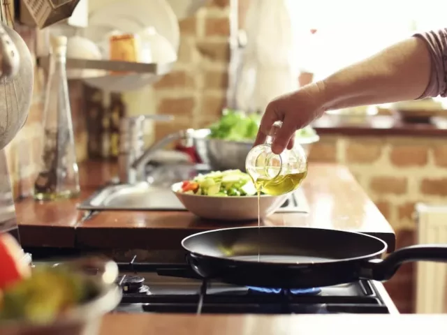 Woman pouring oil with healthy fat into a skillet