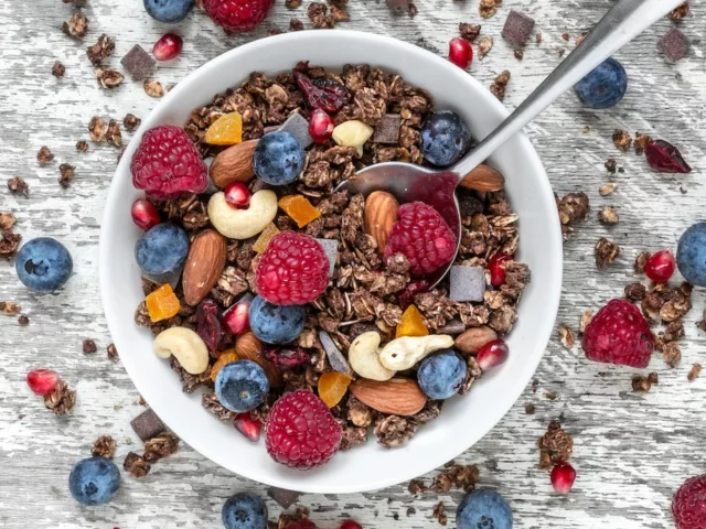 Bowl of granola, cashews, dried fruit, and berries on white wooden table