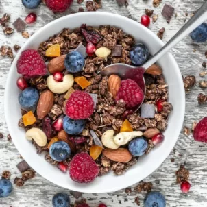 Bowl of granola, cashews, dried fruit, and berries on white wooden table