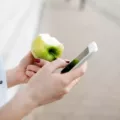 Woman looking at apps on her phone while eating a green apple