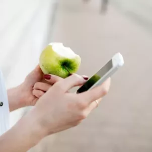 Woman looking at apps on her phone while eating a green apple