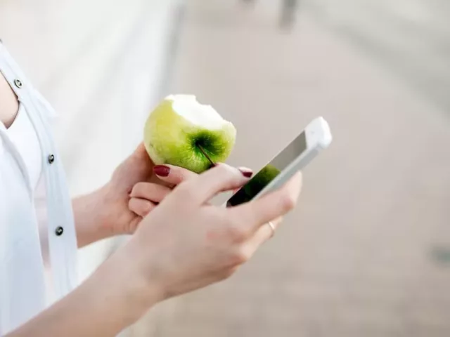 Woman looking at apps on her phone while eating a green apple