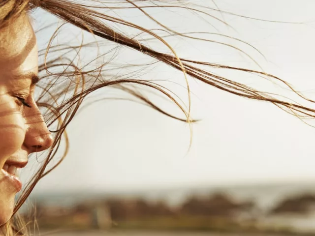 Woman with eyes closed, clear skin, and hair blowing in the summer wind