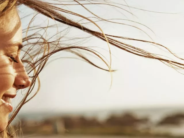 Woman with eyes closed, clear skin, and hair blowing in the summer wind