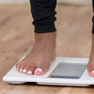 Woman with white pedicure and black leggings looking down to read the scale