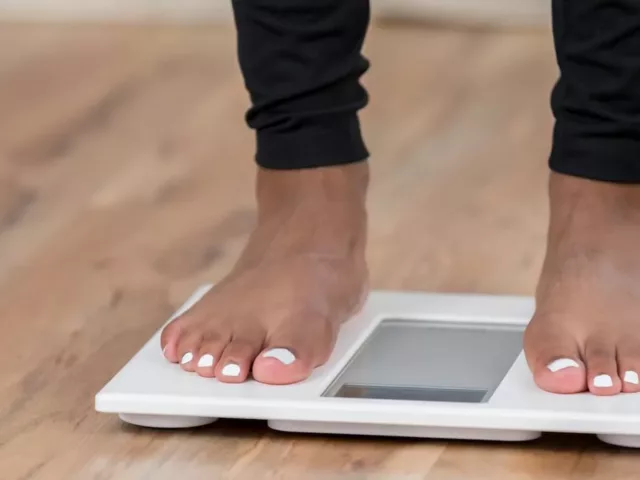 Woman with white pedicure and black leggings looking down to read the scale