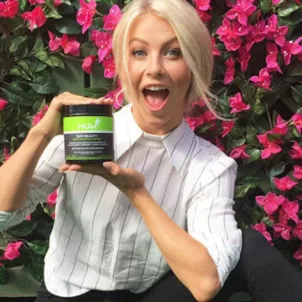 Julianne Hough in front of pink flower wall holding a tub of HUM Nutrition Raw Beauty powder