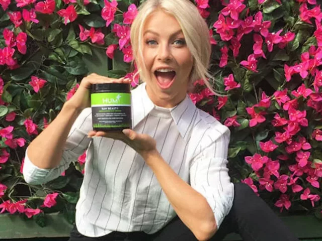 Julianne Hough in front of pink flower wall holding a tub of HUM Nutrition Raw Beauty powder