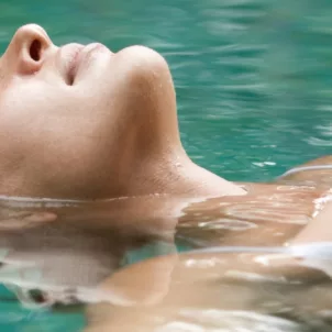 Woman in white bathing suit floating on her back in water