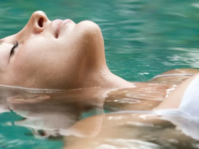 Woman in white bathing suit floating on her back in water
