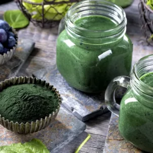 Glass mugs of green juice with raw powder, berries, and spinach