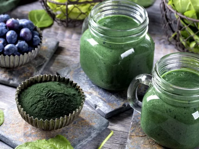 Glass mugs of green juice with raw powder, berries, and spinach