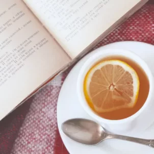 A cup of tea with lemon on a saucer with a book and warm blanket