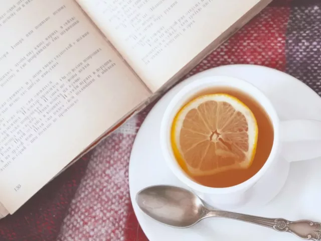 A cup of tea with lemon on a saucer with a book and warm blanket