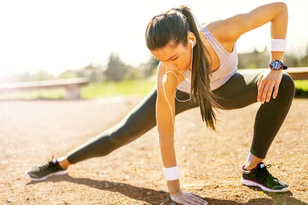 A woman stretching before working out wearing headphones and a fitness tracking watch. 